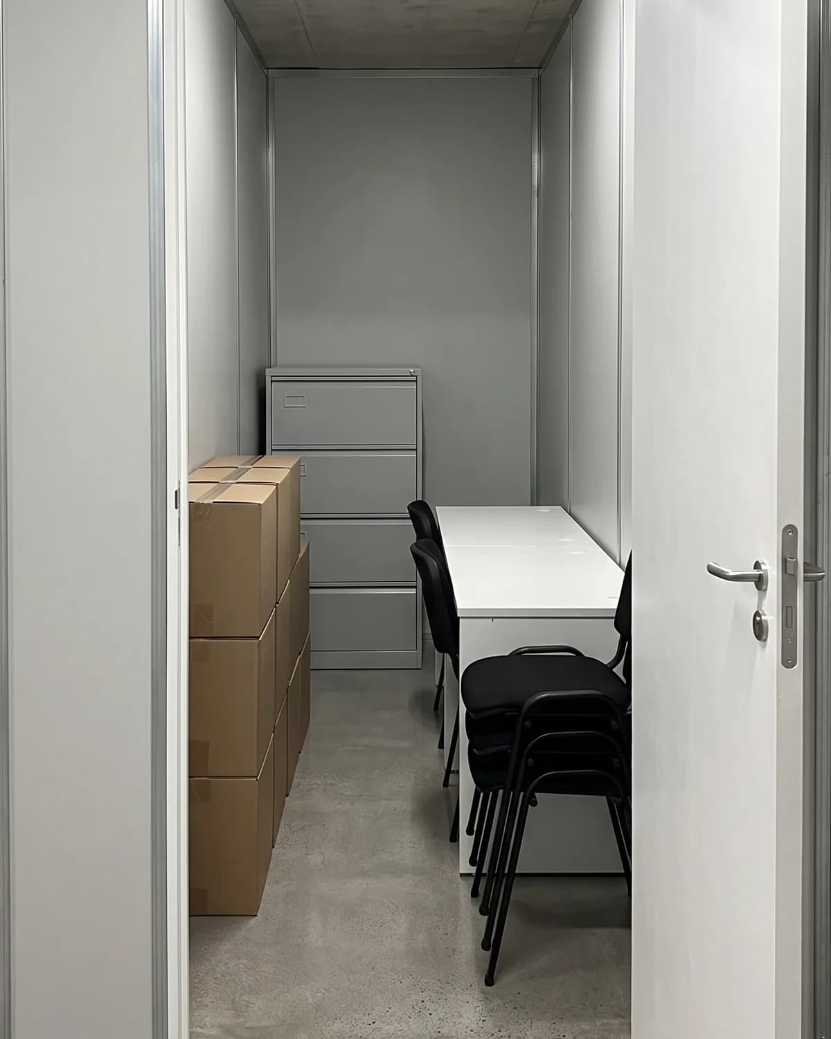 Ilustração do interior de um box grande com mesa, cadeiras, arquivo de aço e caixas