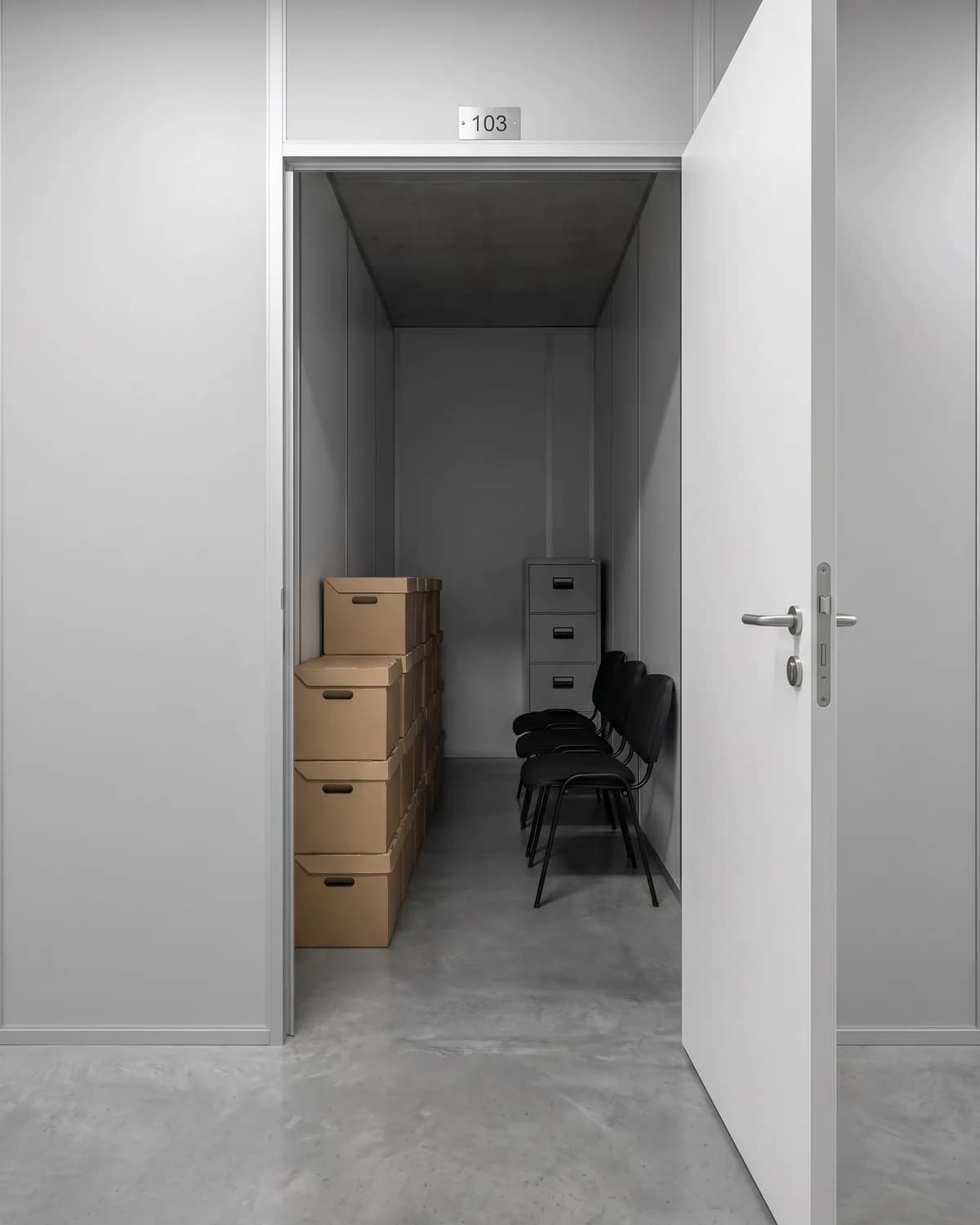 Ilustração do interior de um box médio com caixas-arquivo, cadeiras de escritório e um arquivo de aço