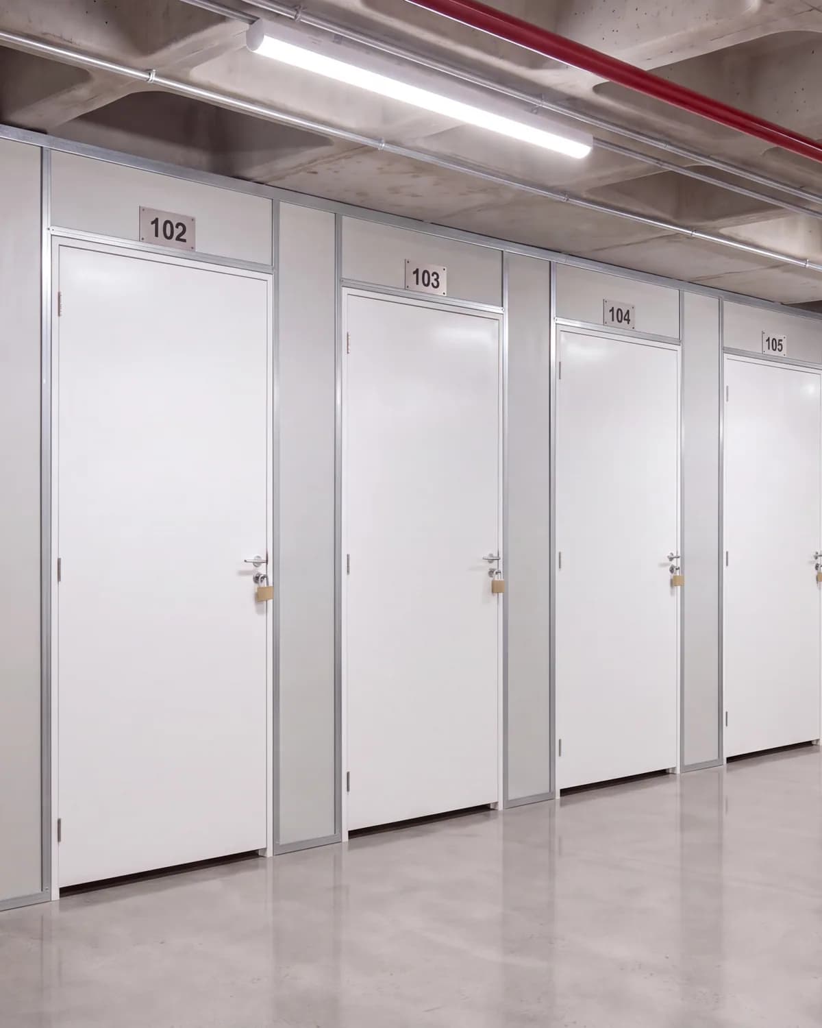 Ilustração de um corredor de boxes com portas brancas de abrir numeradas, piso de concreto polido e laje aparente